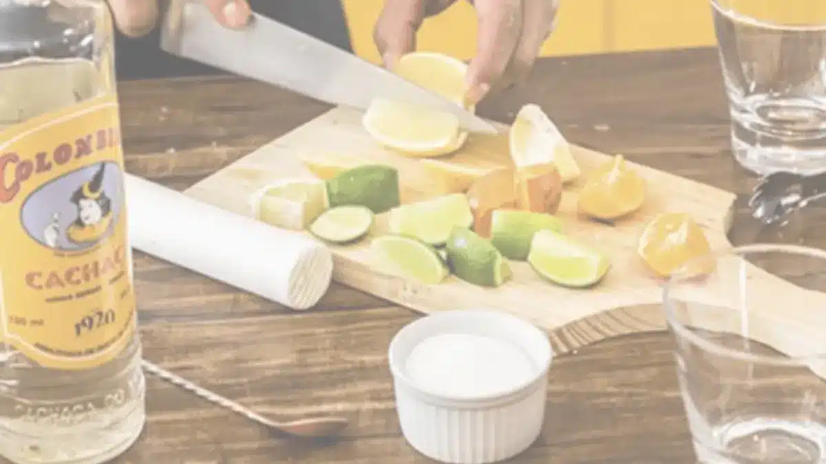 Ingredients for caipirinha cocktail – lime, sugar, cachaça bottle, and ice cubes