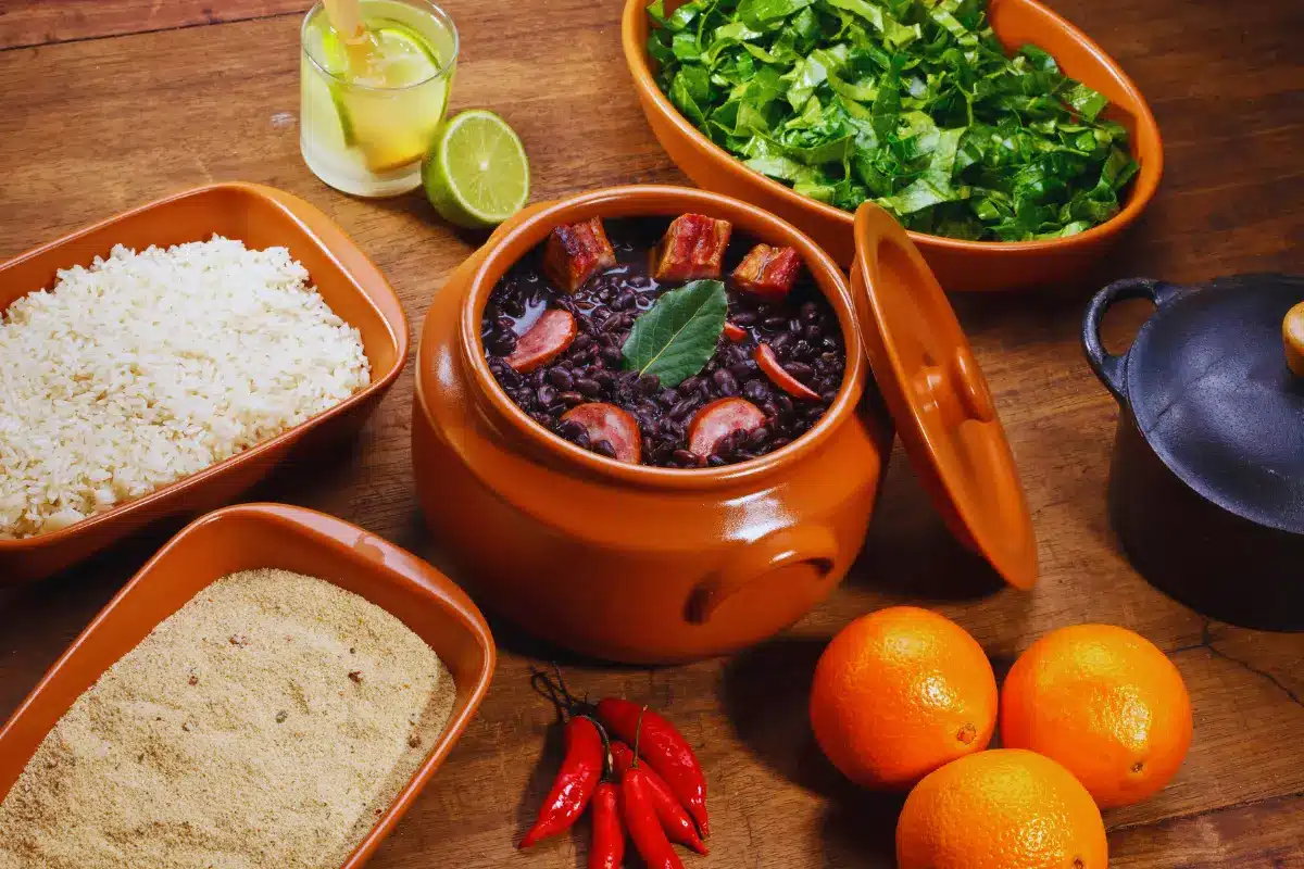 A full feijoada table: the pot of black beans, rice, farofa, collard greens, oranges and a caipirinha.